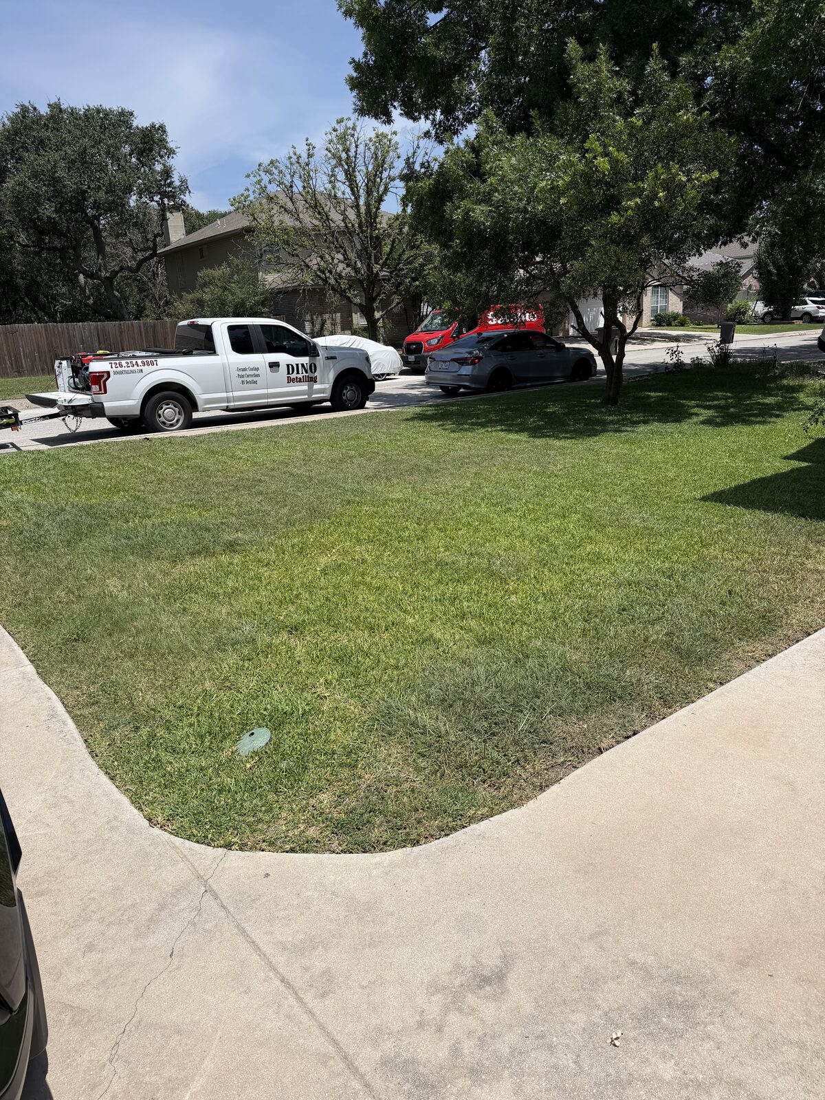 Freshly maintained front lawn with Jurassic Lawn Care service vehicles nearby